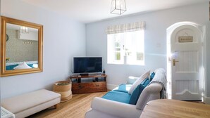 A living room with a television, sofa, and a door labeled "GARDEN". - Prospect Cottage (Stone)