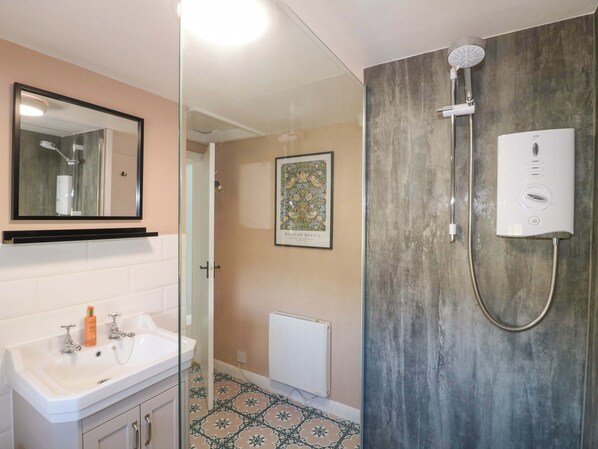 A bathroom with a glass shower enclosure, a white sink with a mirror above it, and a radiator on the wall.