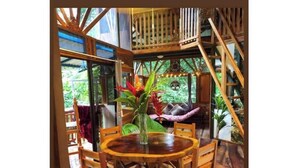 A wooden dining table with chairs, surrounded by a wooden structure with a balcony. - Treehouse with butterfly and exotic fruit farm (Quebrada amarilla)