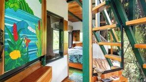 A bedroom with a bed, a window, and a painting of tropical plants. - Treehouse with butterfly and exotic fruit farm (Quebrada amarilla)