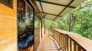 A wooden deck with a railing, a bench, and a covered area with a view of the surrounding forest. - Treehouse with butterfly and exotic fruit farm (Quebrada amarilla)