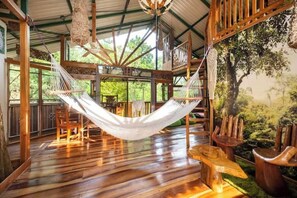 A hammock suspended from a wooden ceiling in a rustic room with wooden floors and furniture. - Treehouse with butterfly and exotic fruit farm (Quebrada amarilla)