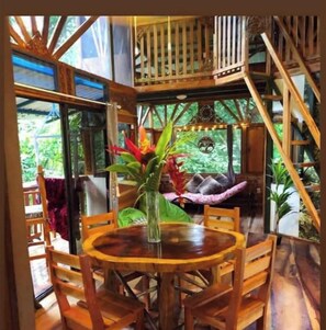 Une table à manger en bois, avec des chaises, entourée d’une structure en bois dotée d’un balcon.