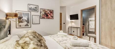 A modern hotel room with a large bed, a flat-screen TV, a vanity with a mirror, and artwork on the walls.