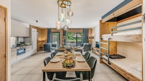 Una habitación moderna y bien iluminada, con una mesa de comedor preparada para cuatro personas, una cama litera y una zona de cocina.