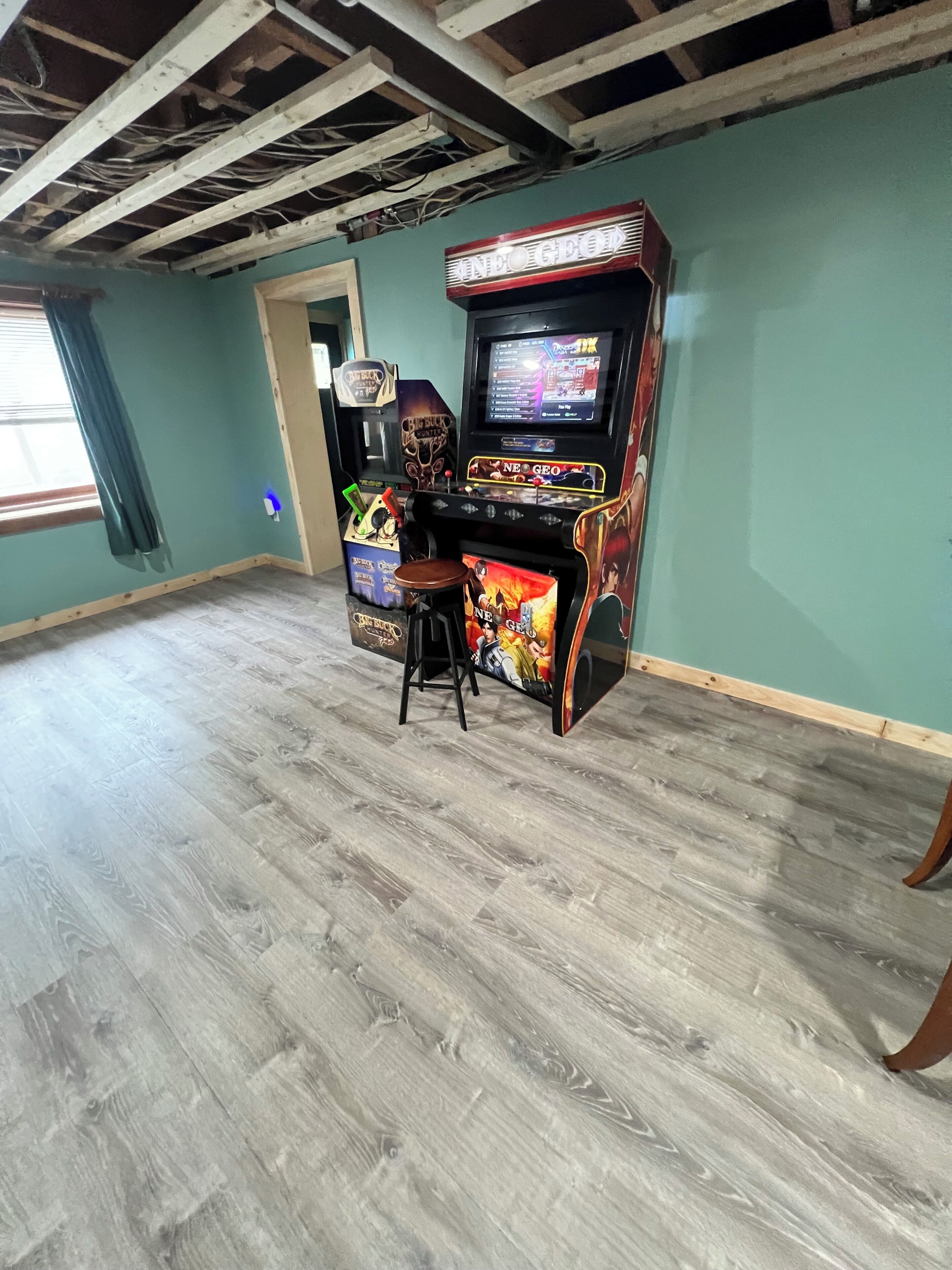 Une pièce avec un plafond en bois, une console de jeux, un tabouret et une fenêtre avec des rideaux.