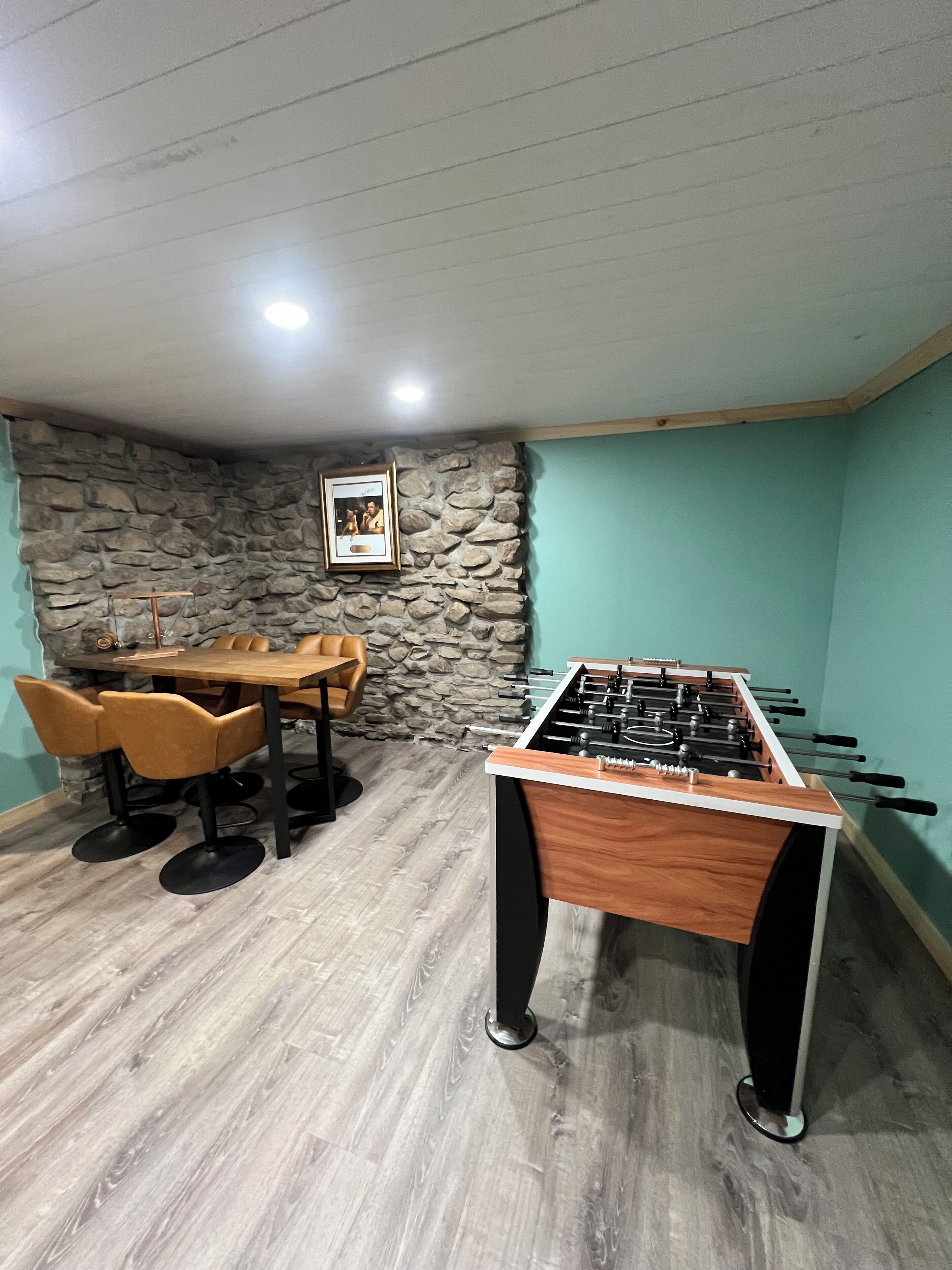 Une pièce avec une table de baby-foot, une table à manger avec des chaises et un mur en pierre.