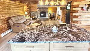A log cabin interior with a stone fireplace, a leather sofa, and a marble countertop. - The Cooperstown Cabin, 8min to All Star Village, 15min to Dreams Park, Sleeps 10 (Oneonta)