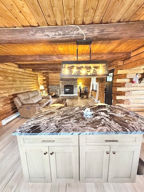 A log cabin interior with a stone fireplace, a leather sofa, and a marble countertop.