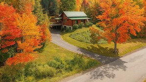 A log cabin with a green roof, surrounded by a well-maintained lawn and autumn-colored trees. - The Cooperstown Cabin, 8min to All Star Village, 15min to Dreams Park, Sleeps 10 (Oneonta)
