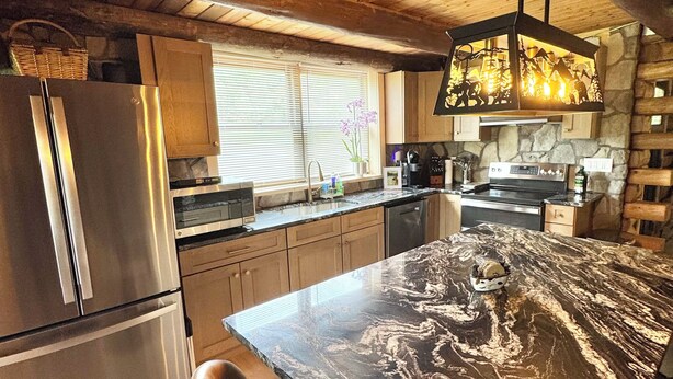 A modern kitchen with a marble countertop, wooden cabinets, a stainless steel refrigerator, and a hanging light fixture. - The Cooperstown Cabin, 8min to All Star Village, 15min to Dreams Park, Sleeps 10 (Oneonta)