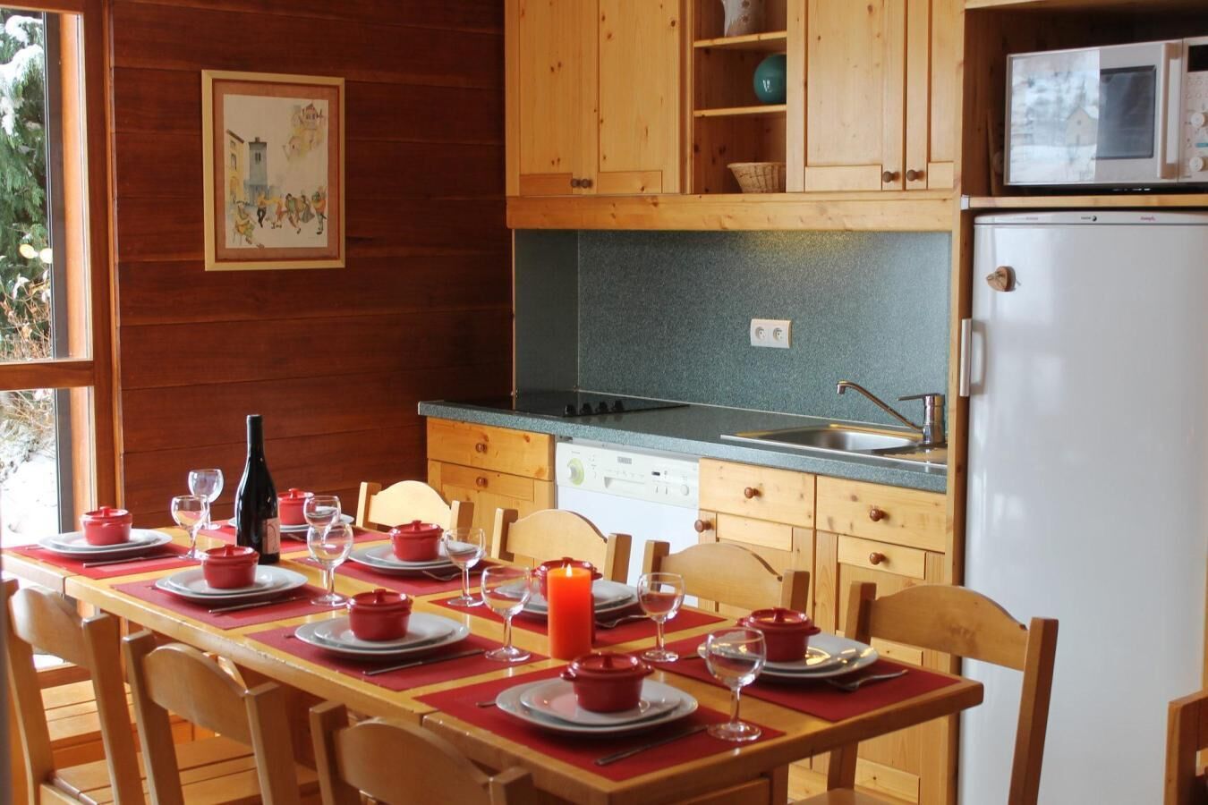 A wooden cabin with a dining area set for four, a kitchen with wooden cabinets, a microwave, and a refrigerator.