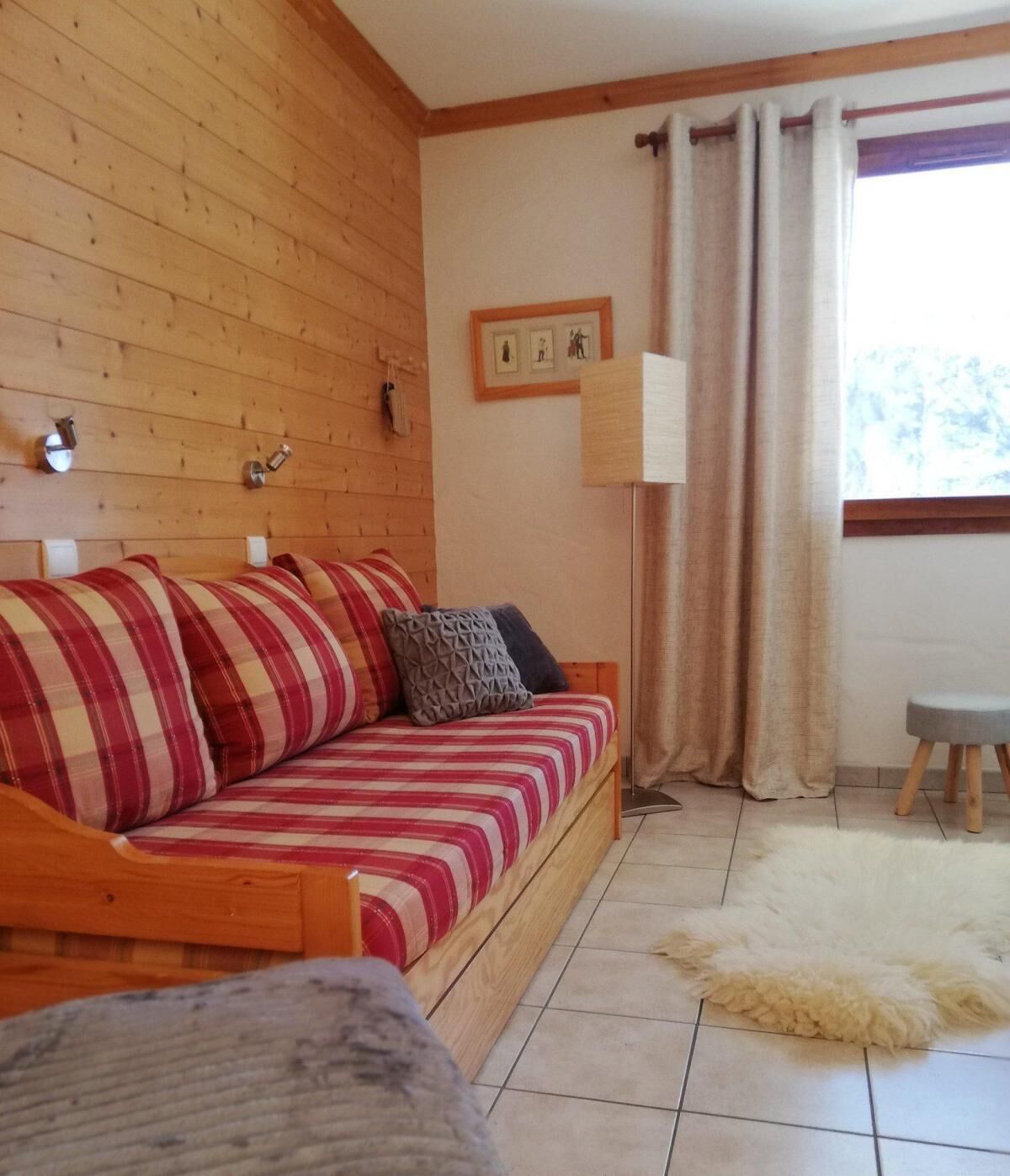 A wooden-paneled room with a sofa, a small stool, a fur rug, and a window with curtains.