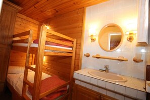 A wooden bunk bed with a red blanket, a white sink, and a mirror above it.