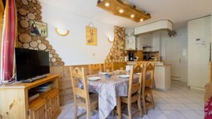 A dining area with a wooden table and chairs, a television on a wooden stand, and a kitchen in the background. - 140m from ski slopes, 3rd floor, balcony, tv, 41m², Valloire (Valloire)