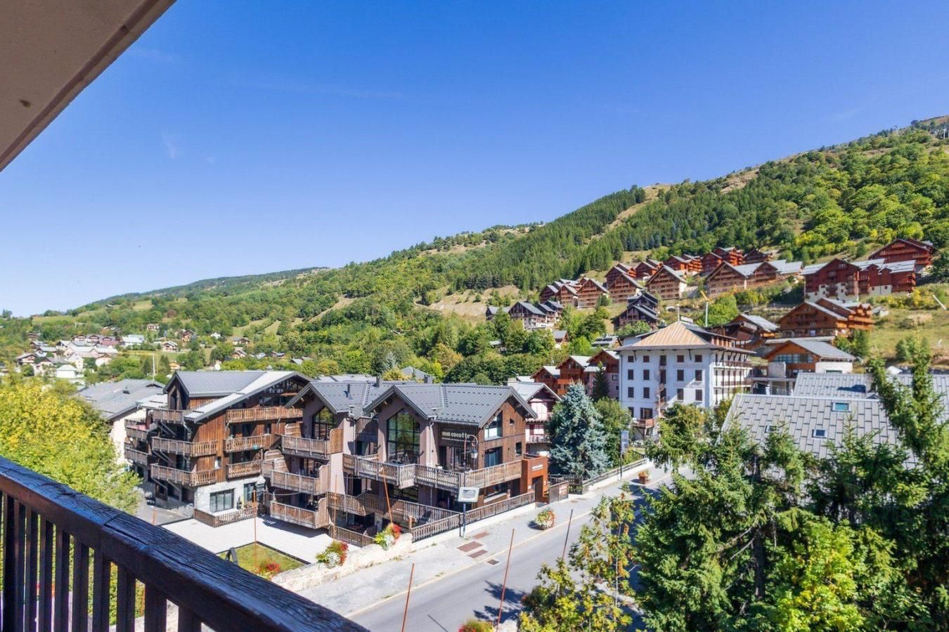 Une station de montagne dotée de chalets en bois et de bâtiments modernes, avec des balcons et une vue dégagée sur les collines environnantes.