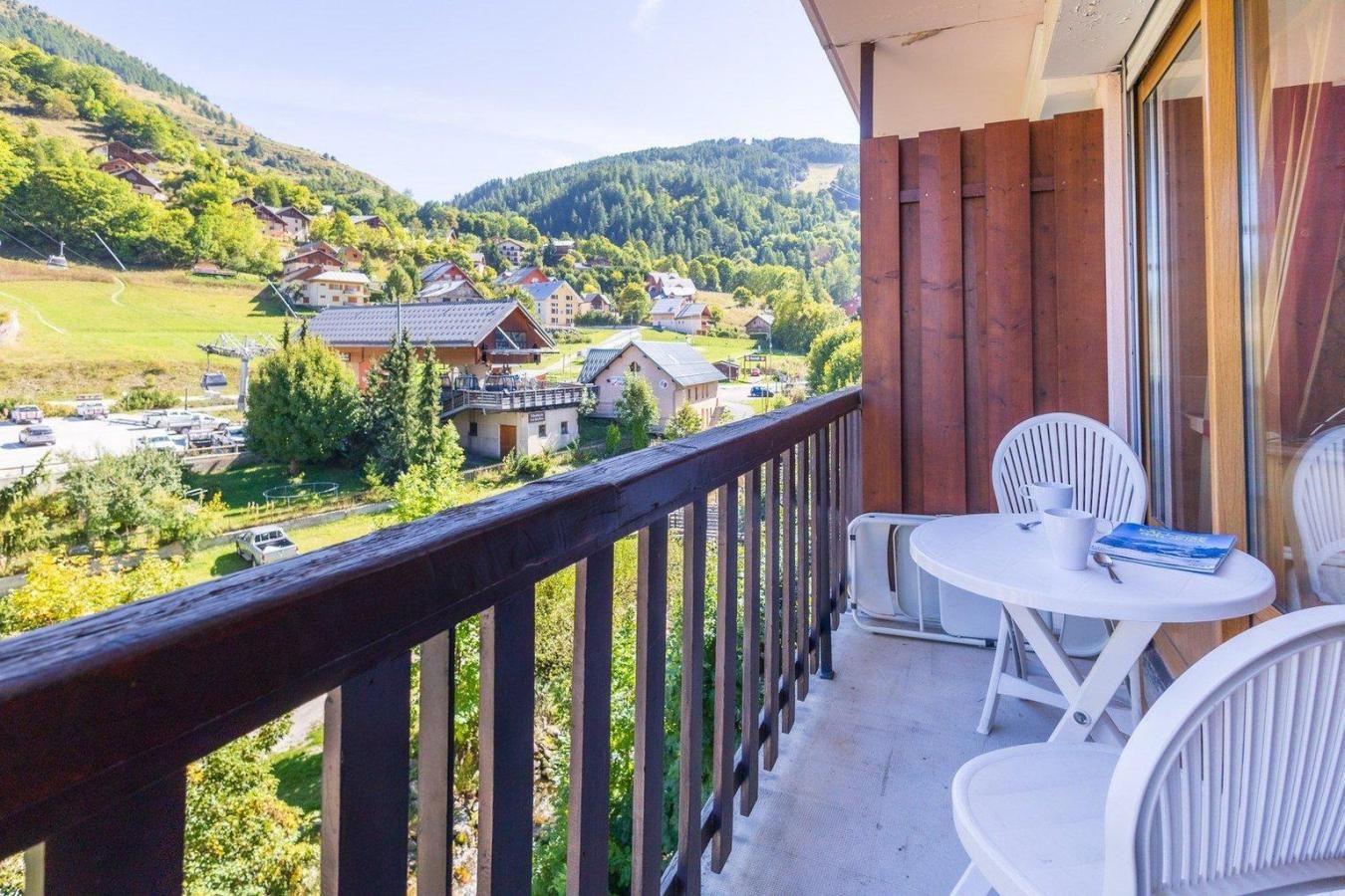 A balcony with a view of a village, a table with chairs, and a book.