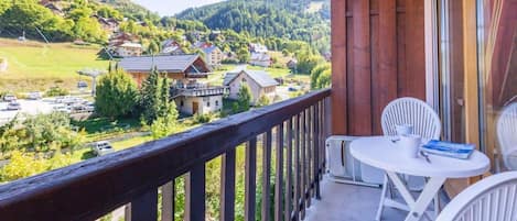 A balcony with a view of a village, a table with chairs, and a book.