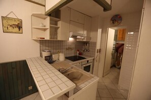 A kitchen with white cabinets, a sink, a stove, and a tiled backsplash. There is a shelf with kitchenware and a sign on the wall.