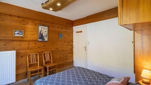 A wooden-paneled room with a bed, two chairs, a radiator, and a door. - 140m from ski slopes, 3rd floor, balcony, tv, 41m², Valloire (Valloire)