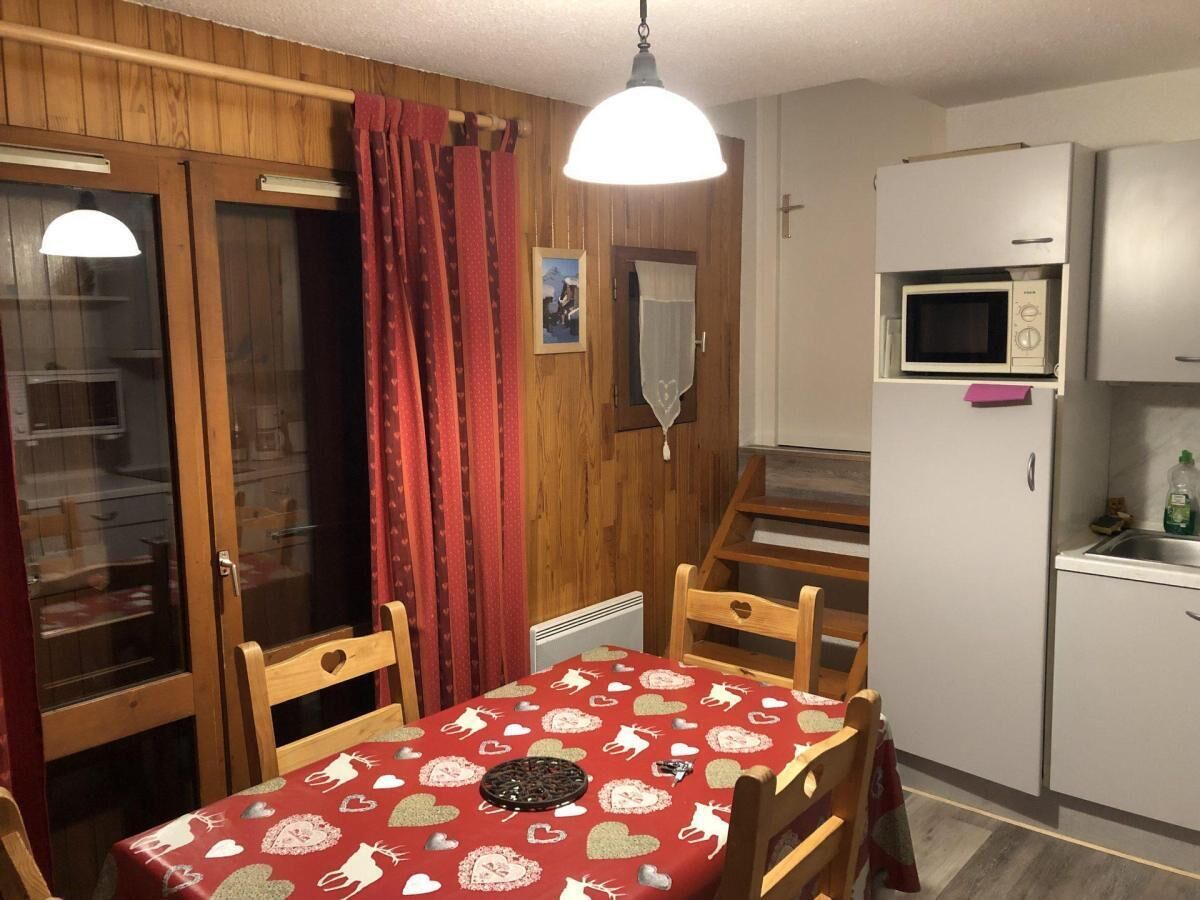 A compact kitchen with a microwave, a small fridge, and a dining table with a red tablecloth.