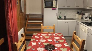 Ett kompakt kök med mikrovågsugn, diskho och ett bord med en röd duk.