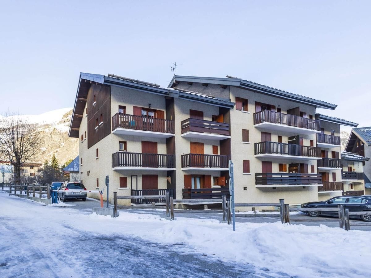 A multi-story hotel with balconies, a ski slope in the background, and a snow-covered ground.