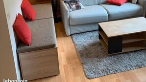 Ein modernes Wohnzimmer mit einem grauen Sofa, roten Kissen, einem Holztisch und einem Bild von einem Reh an der Wand.