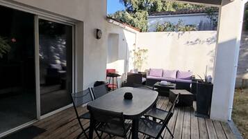 Een terras buiten met een houten terras, een tafel met stoelen en een bank.