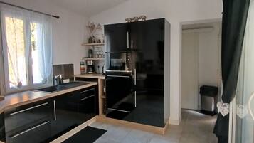 Een moderne keuken met zwarte kastjes, een zwarte koelkast en een zwart aanrecht. Er is een raam met witte gordijnen en een kleine plant op het aanrecht.