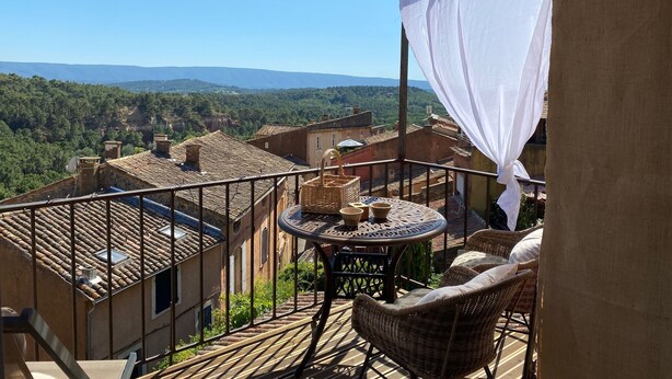A balcony with a table and chairs, overlooking a mountainous landscape. - A balcony overlooking the magnificent ochre cliffs of Roussillon (Roussillon)
