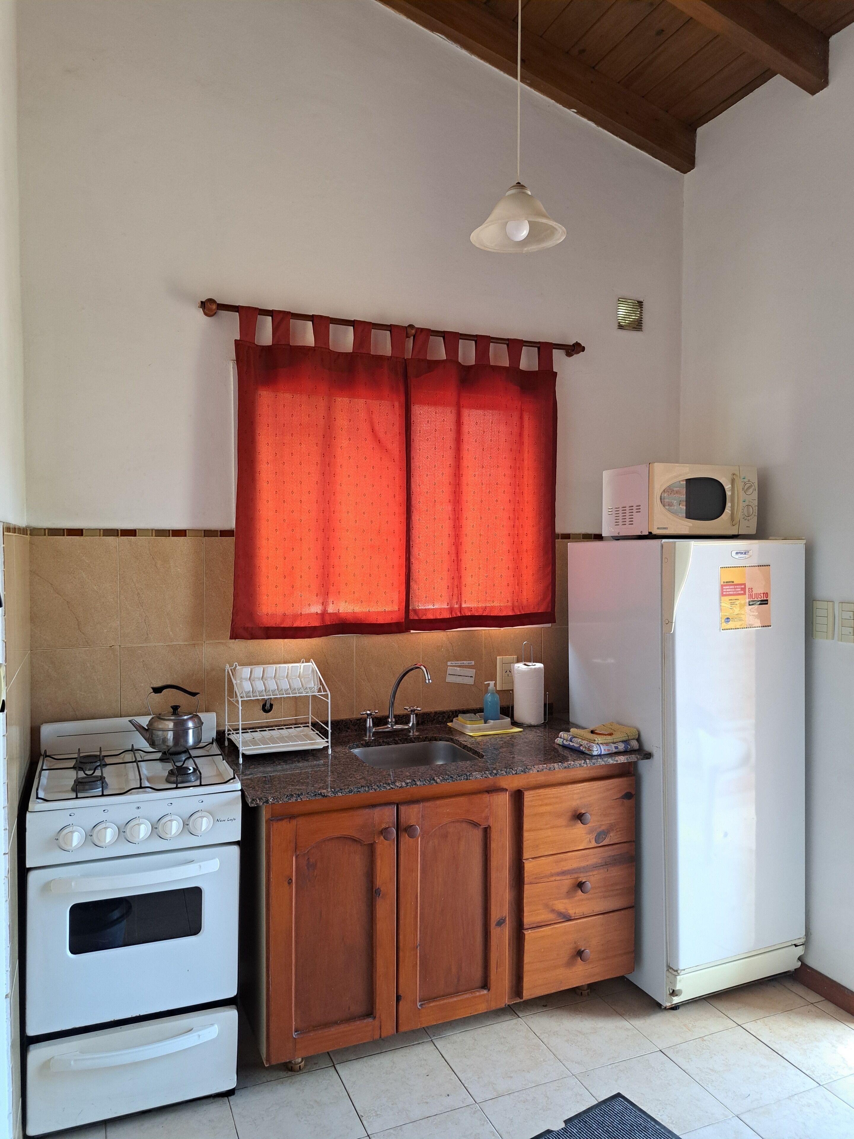 Eine Küche mit Gasherd, Backofen, Holzschränken, Spüle und Kühlschrank.