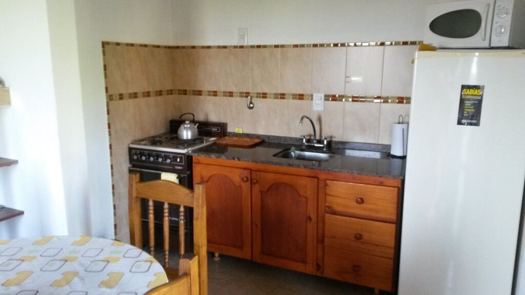 Una cocina compacta con estufa, pileta y refrigerador.