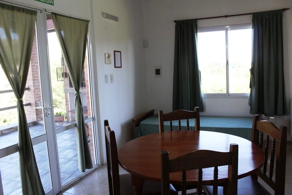 A room with a round wooden table and four chairs, a bench along the window, and a sliding glass door with curtains.
