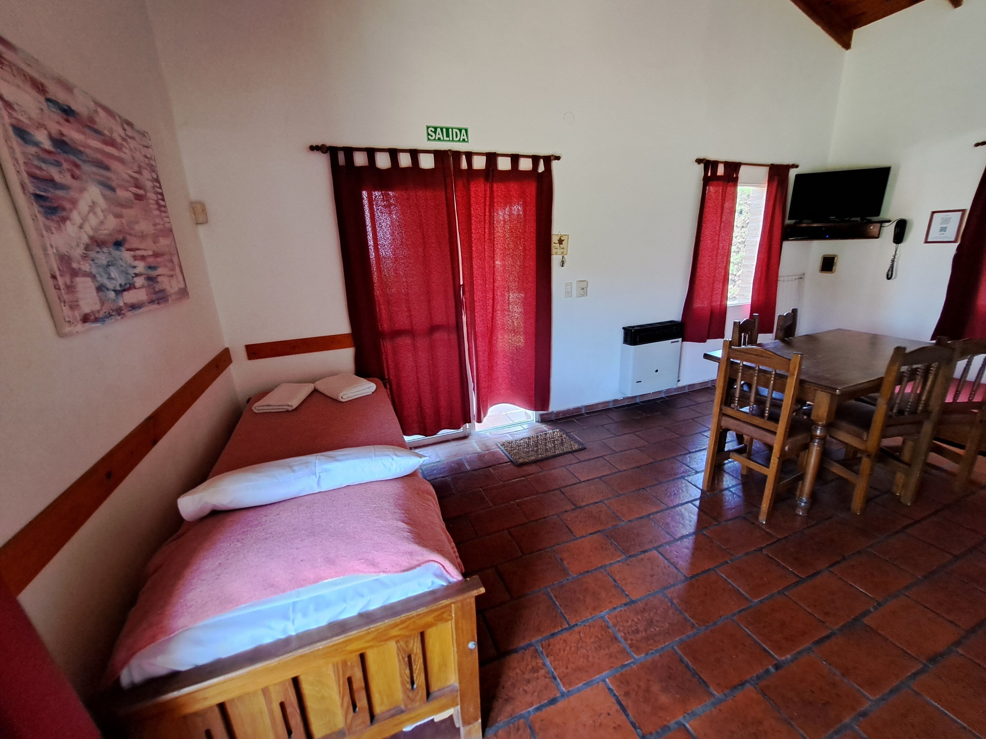 A room with a bed, a table with chairs, a television, and a door marked 'SALIDA'.
