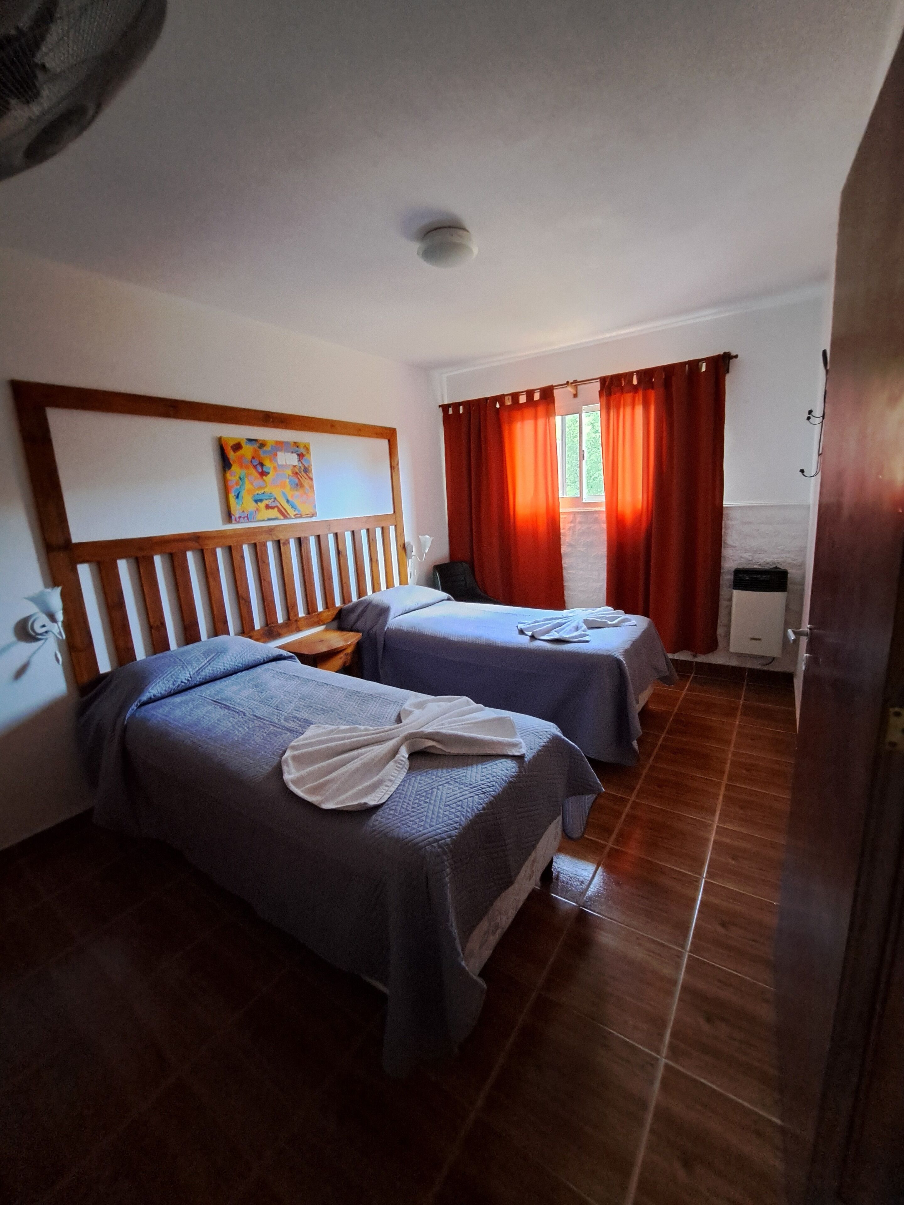 A hotel room with two beds, wooden headboard, a painting on the wall, and a window with curtains.