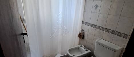 A bathroom with a shower curtain, a bidet, a toilet, and a small rug on the floor.