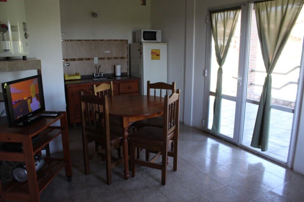 A compact kitchen with a dining area, a TV on a stand, and a refrigerator.