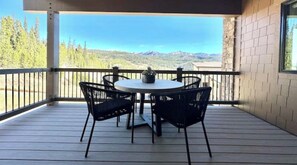 A covered outdoor patio with a round table and four chairs, overlooking a mountainous landscape. - Luxurious Ski-In/Out in Big Sky - Private Hot Tub (Big Sky)