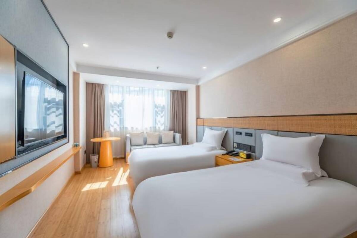 Ein Hotelzimmer mit zwei Betten, einem Fernseher, einem Schreibtisch und einem Vorhangfenster.