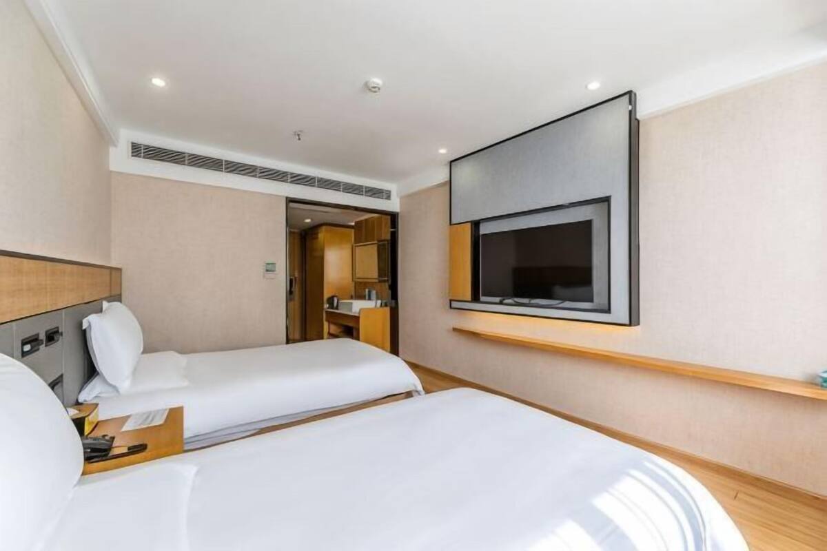 Ein Hotelzimmer mit zwei Betten, einem an der Wand montierten Fernseher und einem kleinen Schreibtisch mit Stuhl.