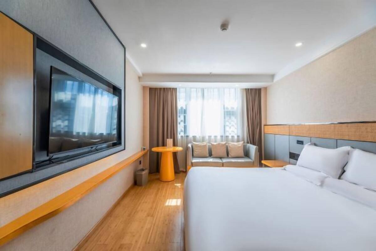 Ein modernes Hotelzimmer mit einem großen Bett, einem an der Wand befestigten Fernseher, einem kleinen runden Tisch und einem Sofa.