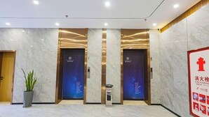 A modern lobby with marble flooring, two elevators, a potted plant, and a fire safety poster. - HUAZHU-StarwayHotel (Shangrao Central Plaza Pedestrian Street store) (Shangrao)