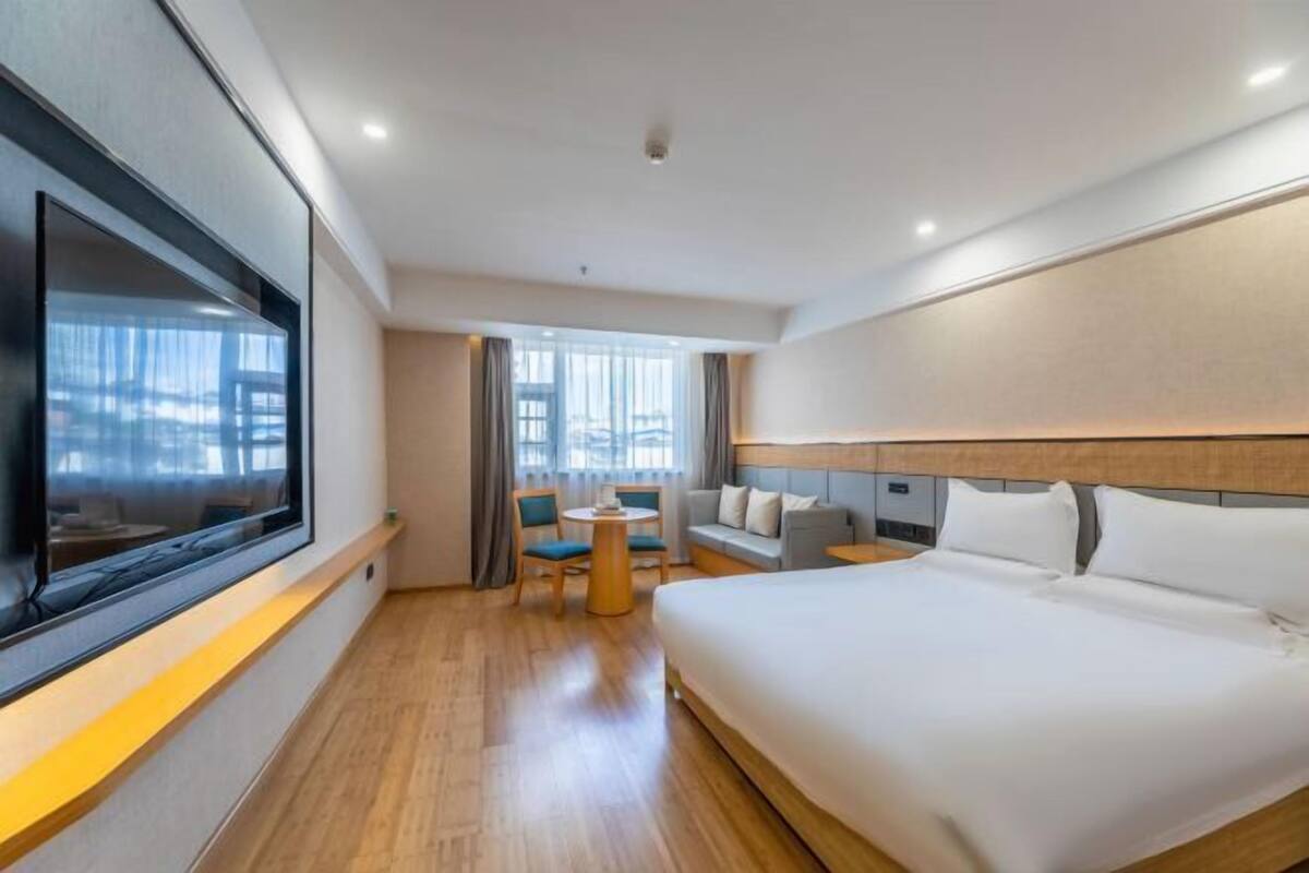 Ein Hotelzimmer mit einem großen Bett, einem an der Wand befestigten Fernseher, einem kleinen Tisch mit Stühlen und einer Couch.