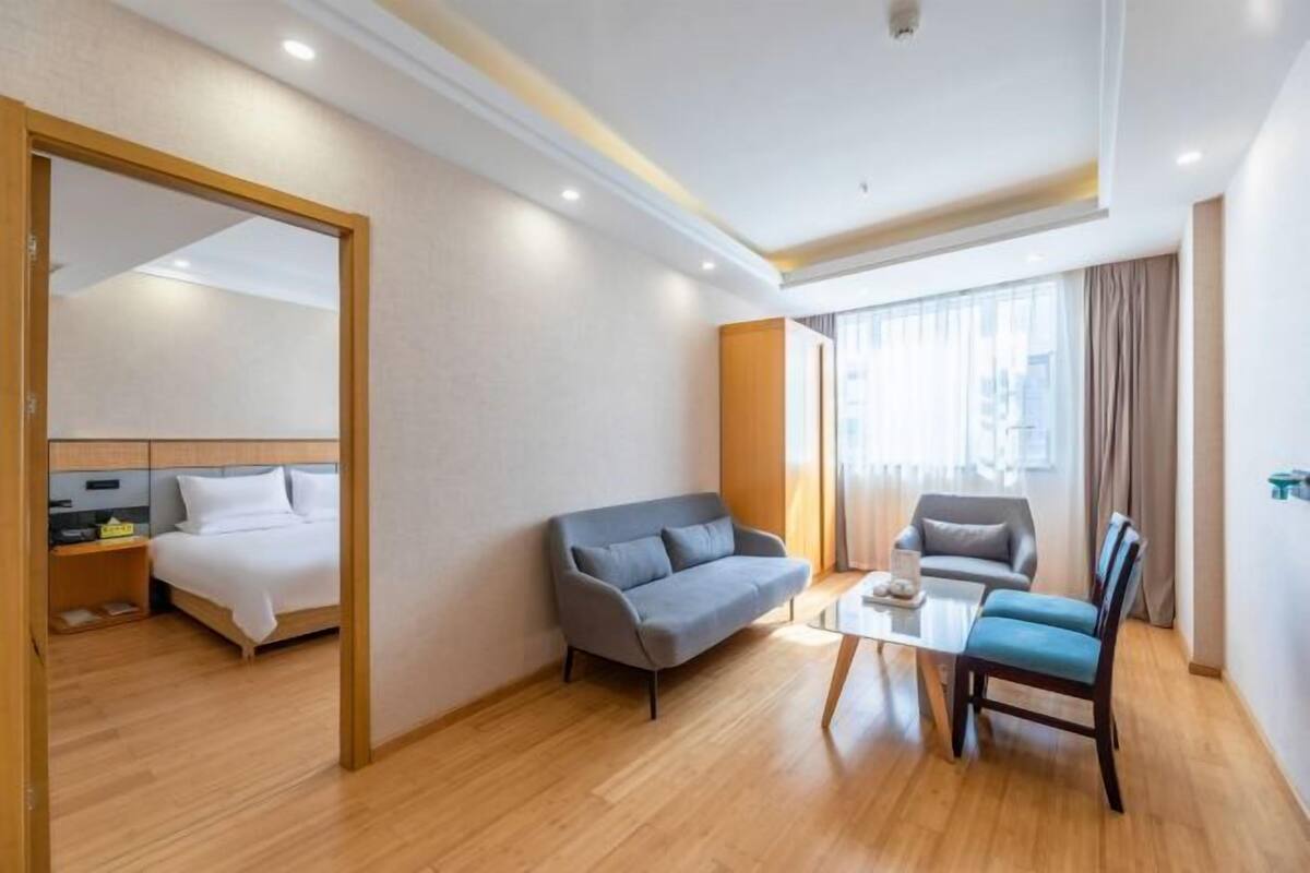Ein Hotelzimmer mit einem Bett, einem Sofa, einem Sessel, einem kleinen Tisch und einem großen Fenster mit Vorhängen.