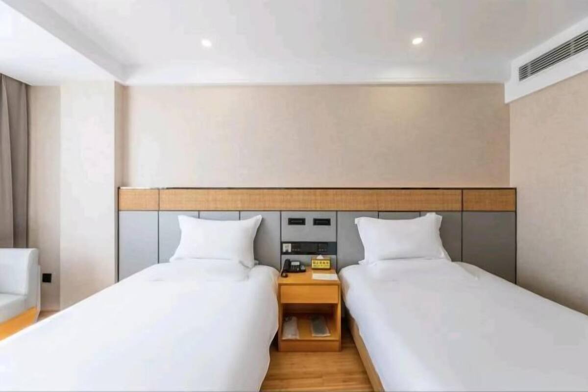 Ein Hotelzimmer mit zwei Einzelbetten, einem Holfnachtkästchen, einem kleinen Tisch und einem Sofa.