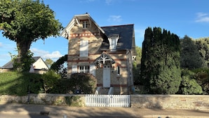 Una casa de piedra con cerca blanca, una chimenea y un árbol grande en el frente.