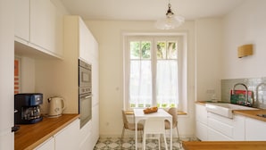 Una cocina compacta con encimera de madera, armarios blancos, cafetera, hervidor y ventana con cortinas.