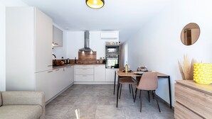 A modern kitchen with white cabinets, a wooden dining table, and a built-in oven. - L'Île de Beauté - Climatisé (Pietrosella)