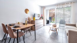 A modern dining area with a wooden table, cushioned chairs, and a kitchen area with a TV. - L'Île de Beauté - Climatisé (Pietrosella)